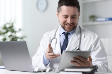 Smiling doctor having online consultation via tablet at table in clinic