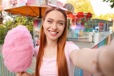 Photo of Happy woman with cotton candy taking selfie at funfair