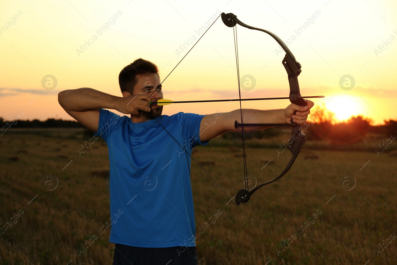 Photo of Man with bow and arrow practicing archery in field at sunset