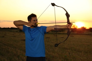 Photo of Man with bow and arrow practicing archery in field at sunset