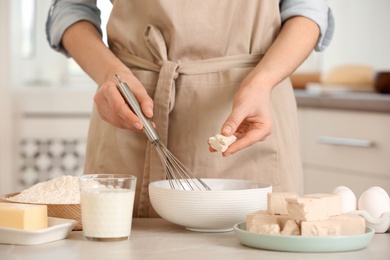 Woman adding compressed yeast for preparing dough at table indoors, closeup