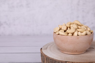 Photo of Tasty cashew nuts in bowl on white wooden table, space for text