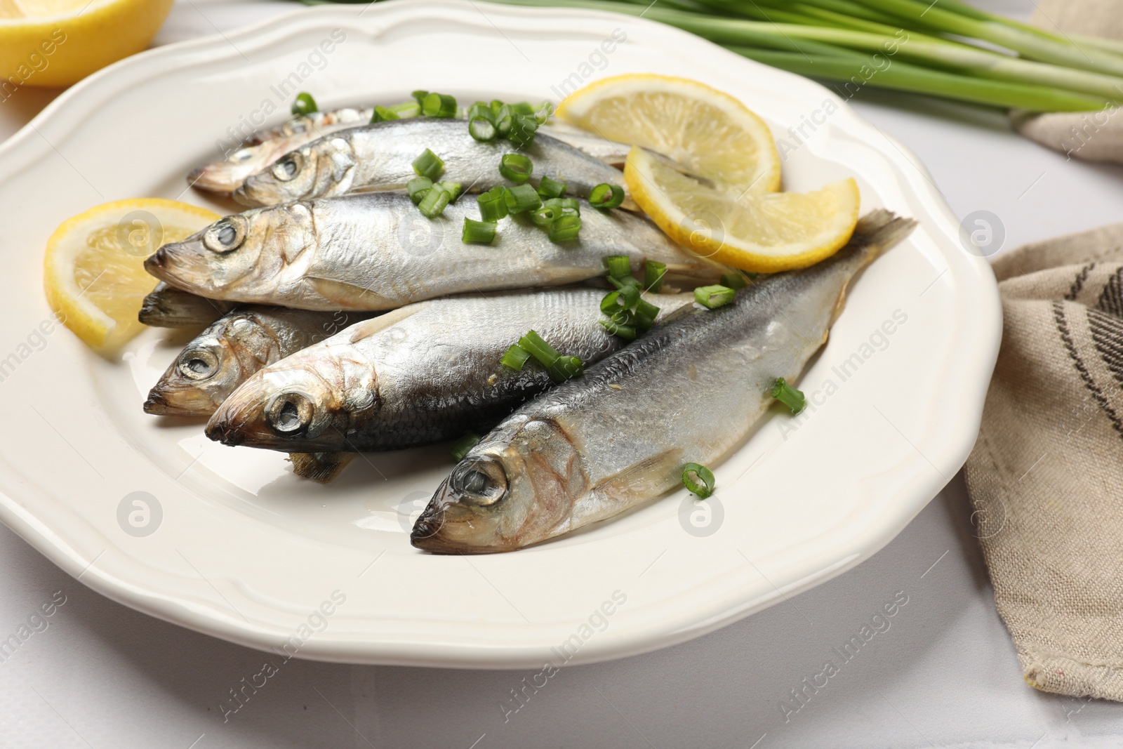 Photo of Fresh raw sprats, green onion and cut lemon on white table, closeup