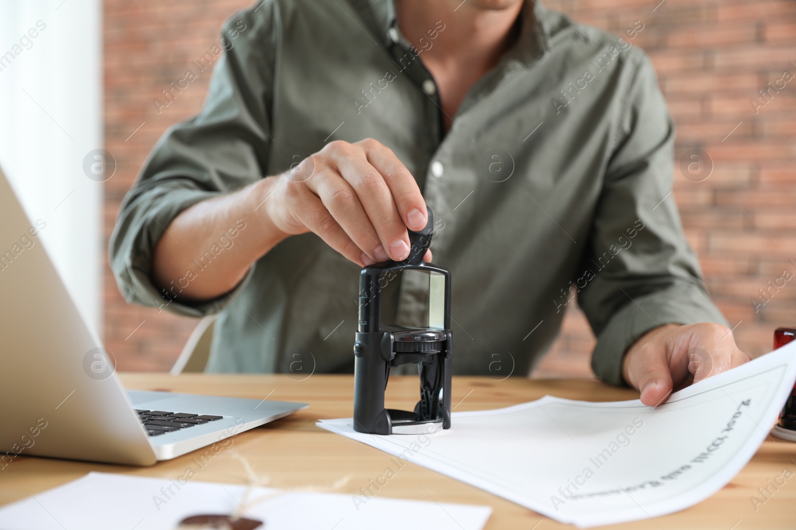 Photo of Male notary stamping document at table in office, closeup