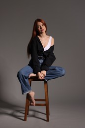 Photo of Beautiful young woman sitting on stool against gray background