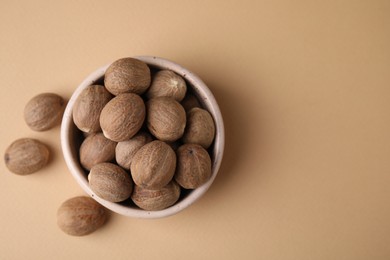 Photo of Whole nutmegs in bowl on light brown background, top view. Space for text
