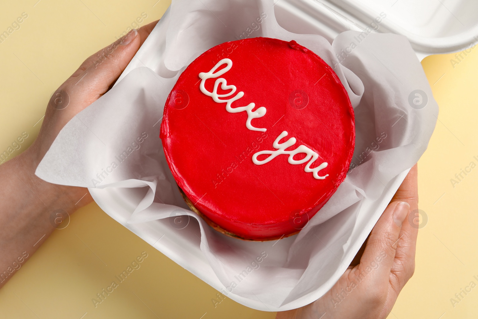 Photo of Woman holding takeaway box with bento cake at beige table, top view. St. Valentine's day surprise