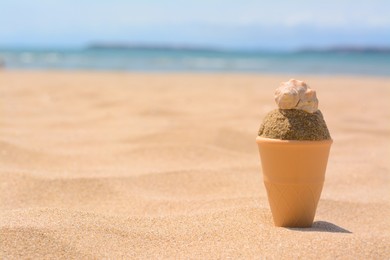 Photo of Plastic ice cream shaped mold with ball of sand and seashell on beach. Space for text