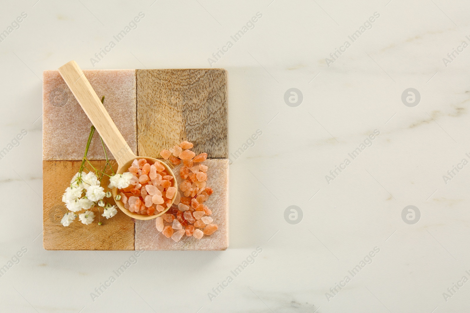 Photo of Orange sea salt and beautiful flowers on white marble table, top view. Space for text