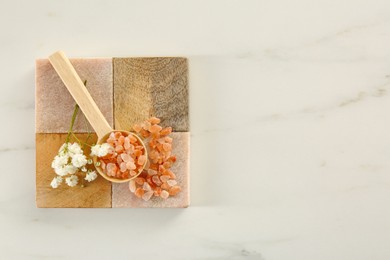 Orange sea salt and beautiful flowers on white marble table, top view. Space for text