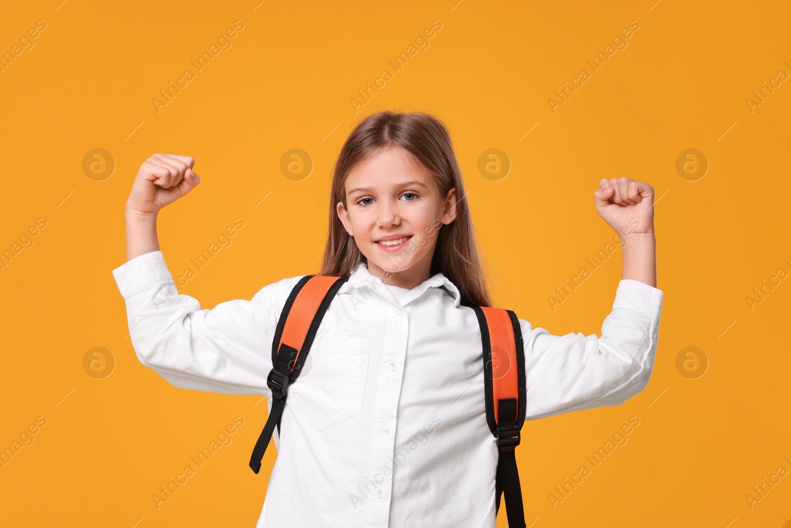 Photo of Happy schoolgirl with backpack on orange background