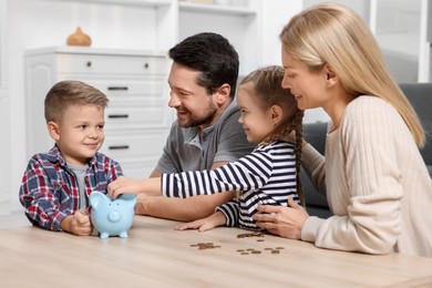 Photo of Family budget. Little boy putting coin into piggy bank while his parents and sister watching indoors