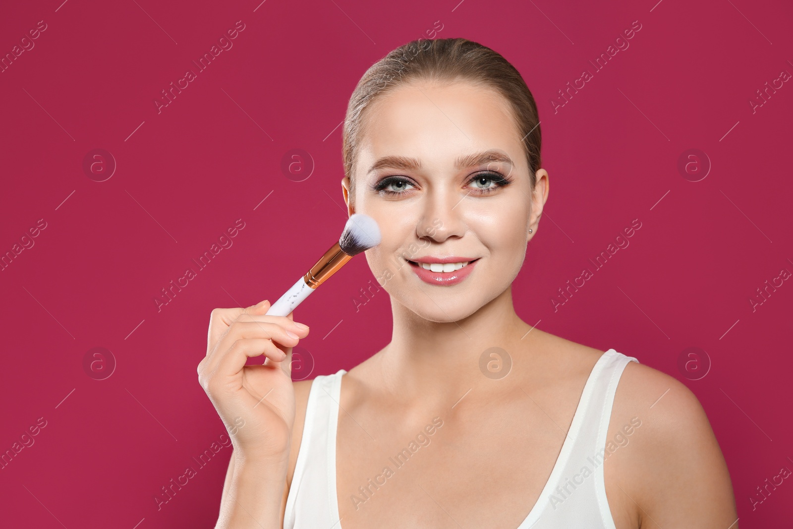 Photo of Beautiful woman applying makeup with brush on pink background