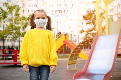 Little girl with medical face mask on playground during covid-19 quarantine