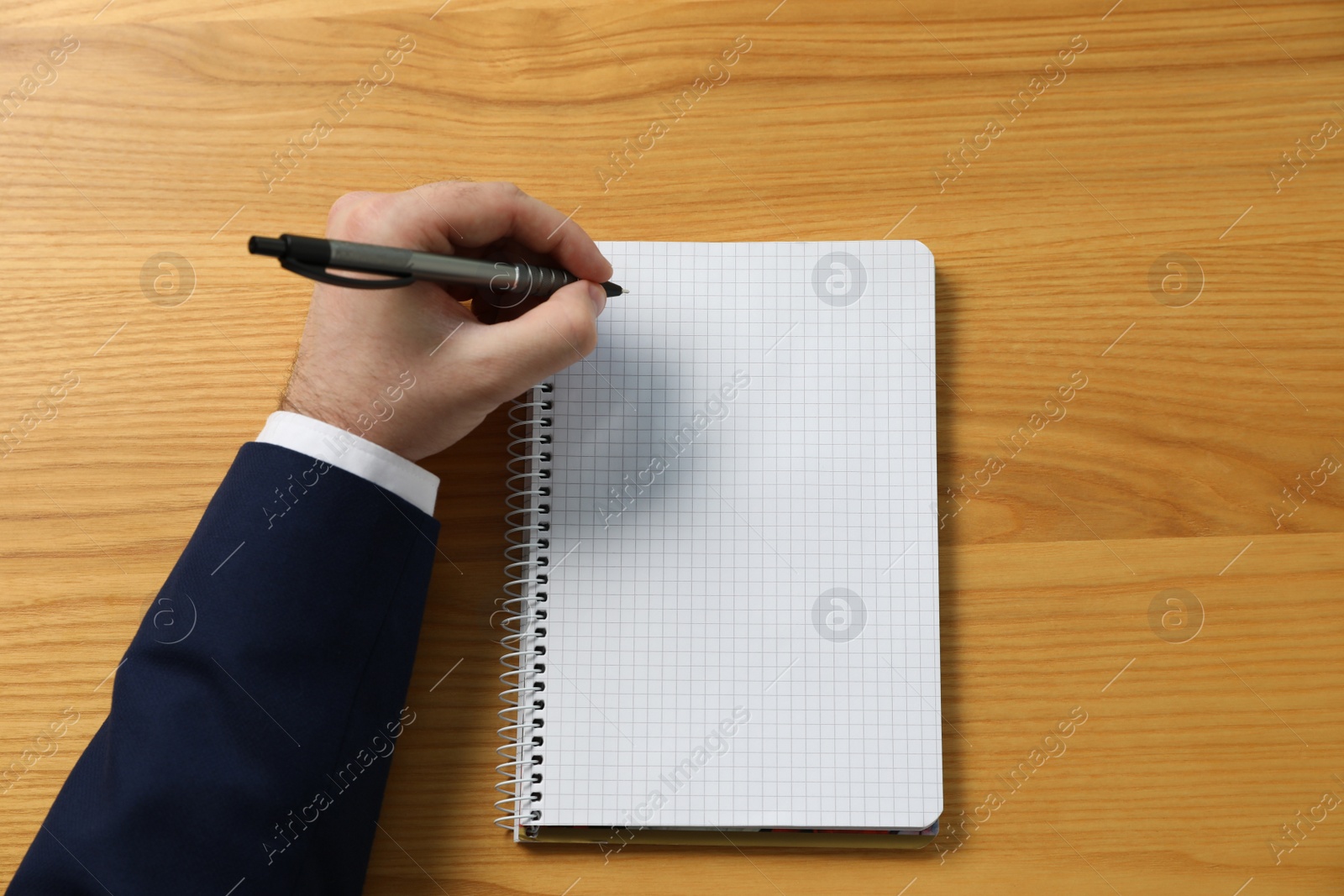 Photo of Left-handed man writing in notebook at wooden desk, top view