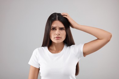 Emotional woman examining her hair and scalp on grey background. Dandruff problem