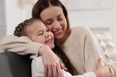 Happy mother hugging her cute daughter on sofa at home