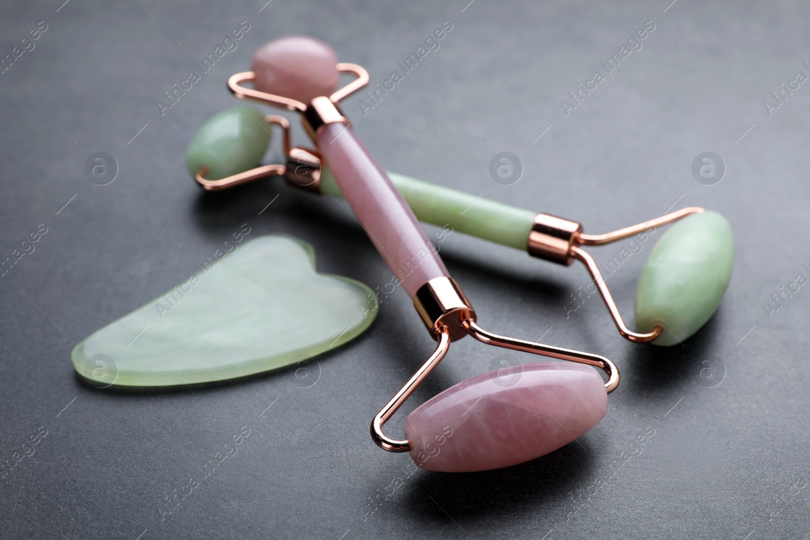 Photo of Quartz gua sha tool and face rollers on grey table, closeup