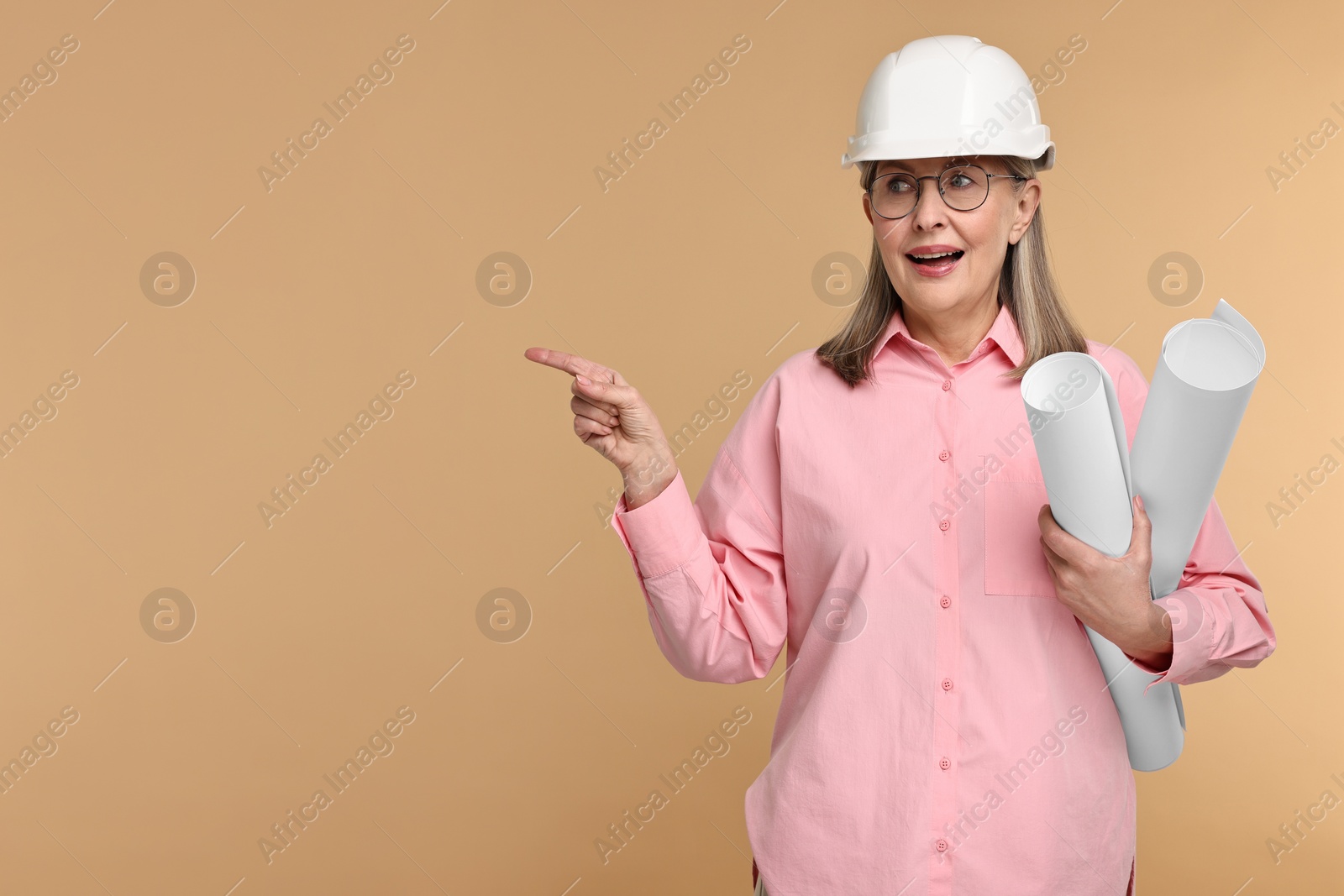 Photo of Architect in hard hat with drafts pointing at something on beige background, space for text