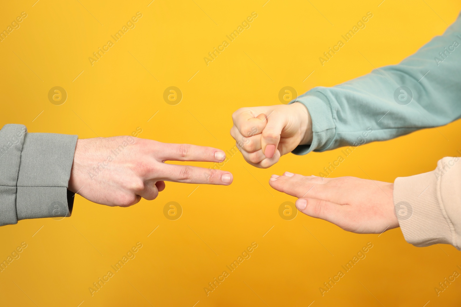 Photo of People playing rock, paper and scissors on orange background, closeup