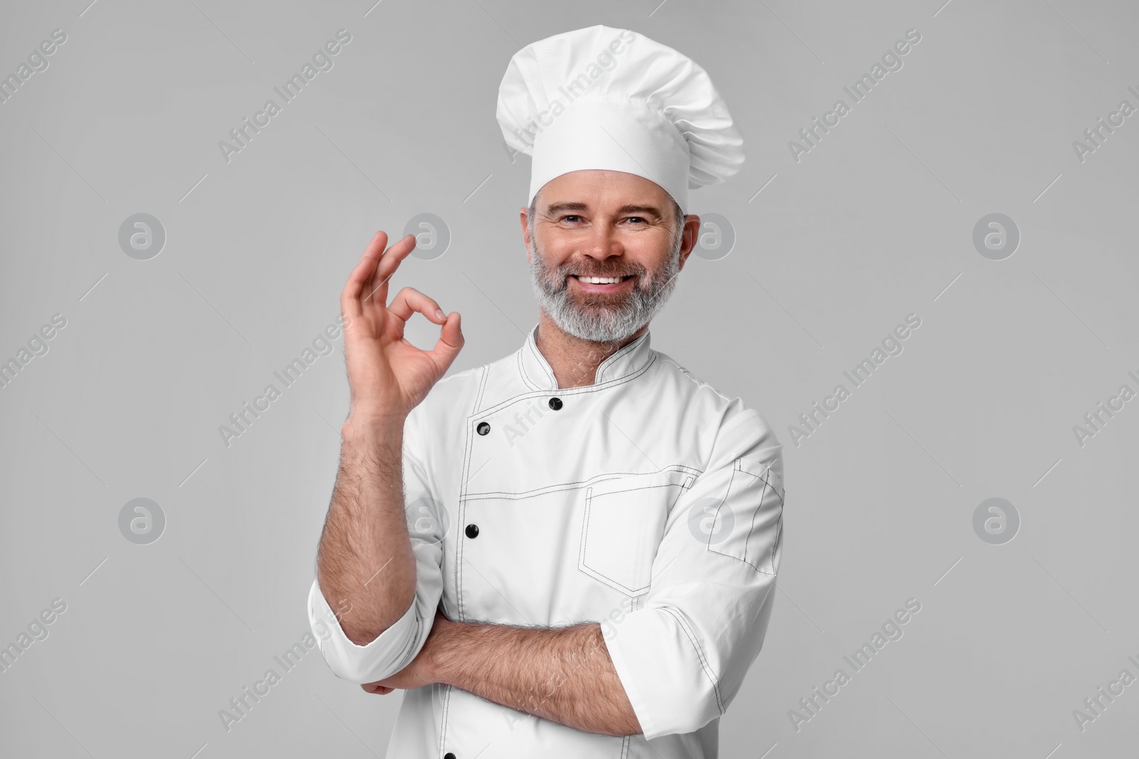 Photo of Happy chef in uniform showing OK gesture on grey background