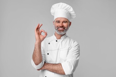 Happy chef in uniform showing OK gesture on grey background