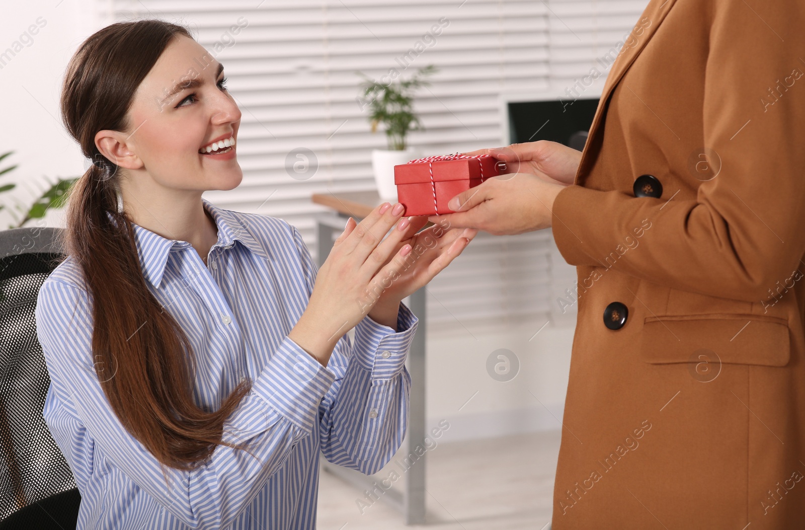 Photo of Woman presenting gift to her colleague in office