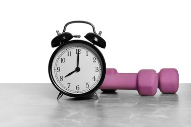 Alarm clock and dumbbells on marble table against grey background. Morning exercise