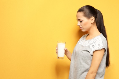 Young woman with dairy allergy holding glass of milk on color background