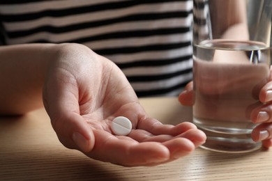 Photo of Woman with glass of water and pill at wooden table, closeup