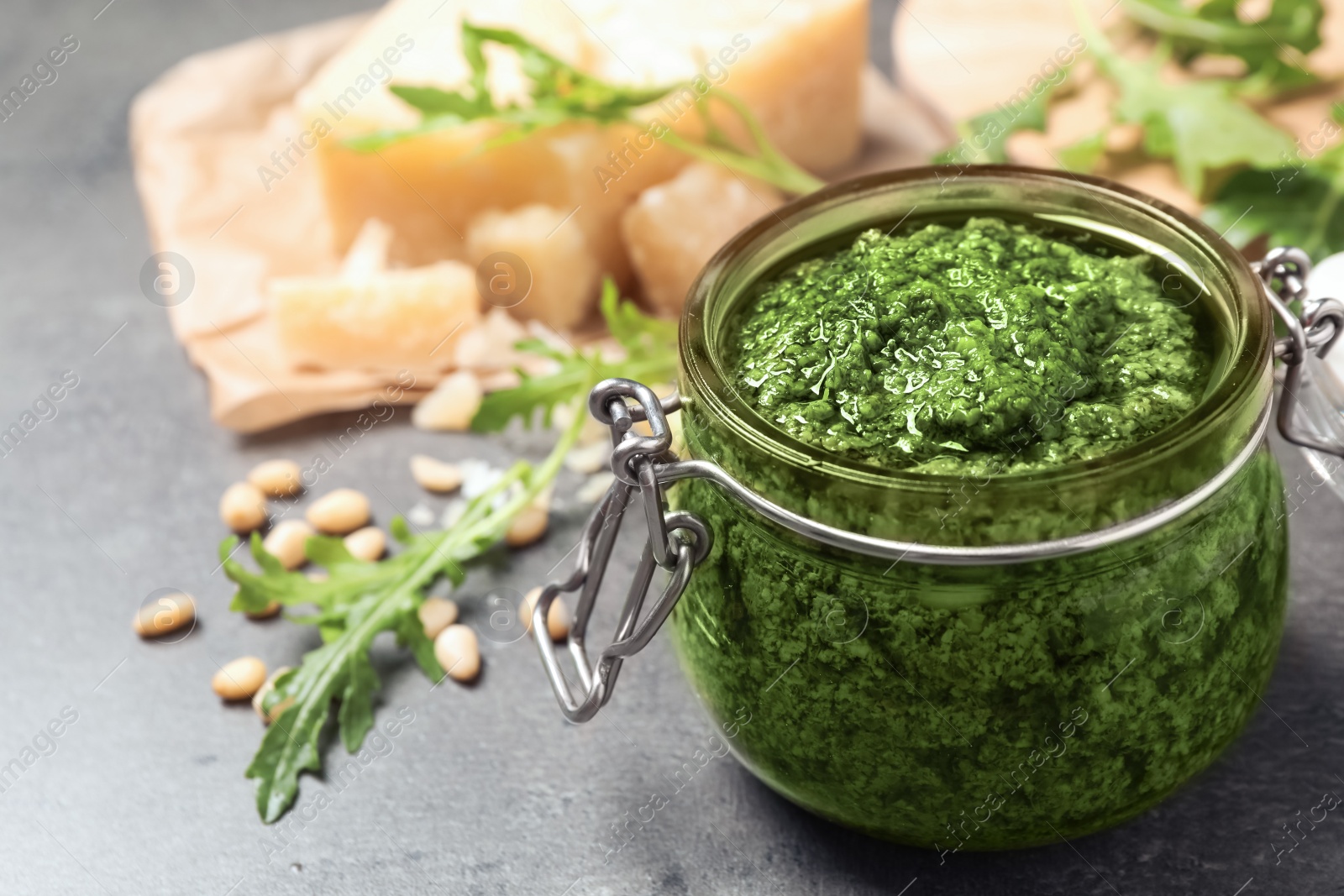 Photo of Jar of tasty arugula pesto and ingredients on grey table