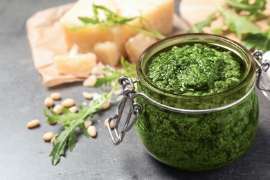 Photo of Jar of tasty arugula pesto and ingredients on grey table