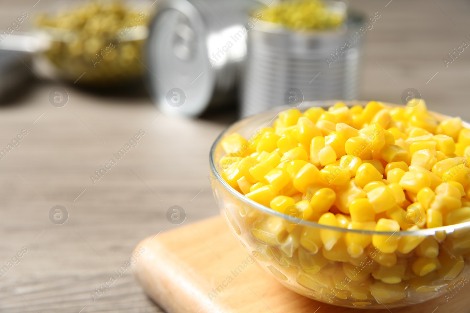 Photo of Glass bowl of canned sweet corn on wooden table, closeup. Space for text