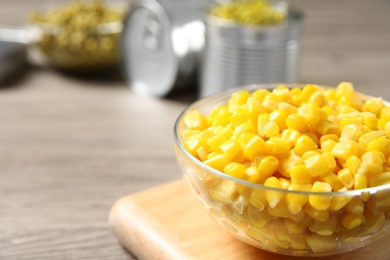 Photo of Glass bowl of canned sweet corn on wooden table, closeup. Space for text