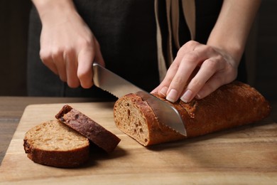 Photo of Woman cutting freshly baked rye baguette at wooden table, closeup