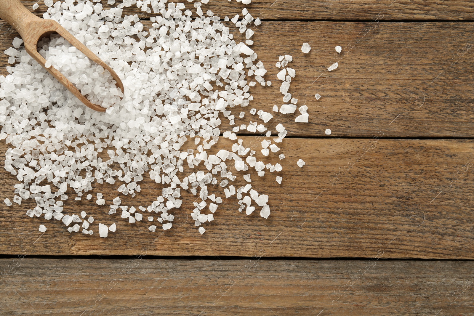 Photo of Natural sea salt and scoop on wooden table, flat lay. Space for text