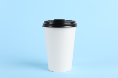 Paper cup with plastic lid on light blue background. Coffee to go