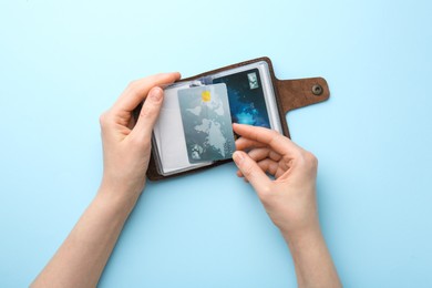 Woman holding leather card holder with credit cards on light blue background, top view