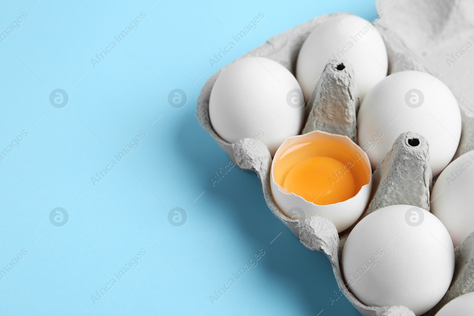 Photo of Fresh chicken eggs in box on light blue background, closeup. Space for text