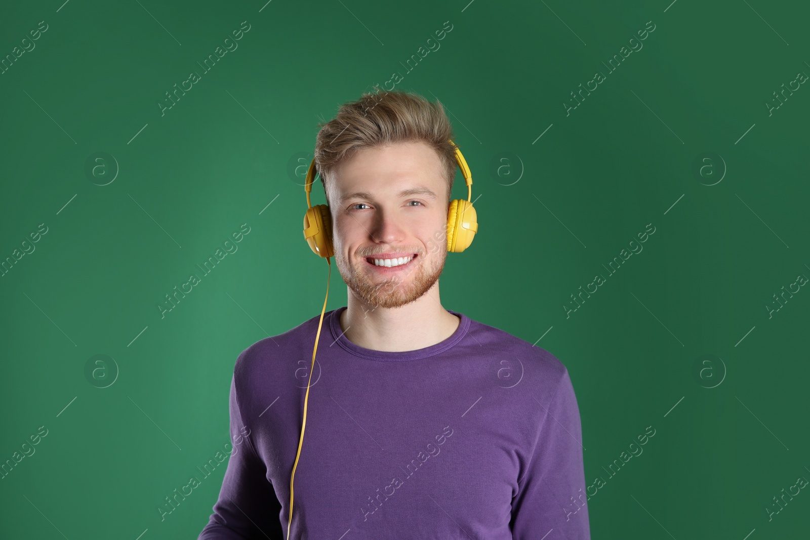 Photo of Handsome young man listening to music with headphones on color background