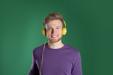 Photo of Handsome young man listening to music with headphones on color background