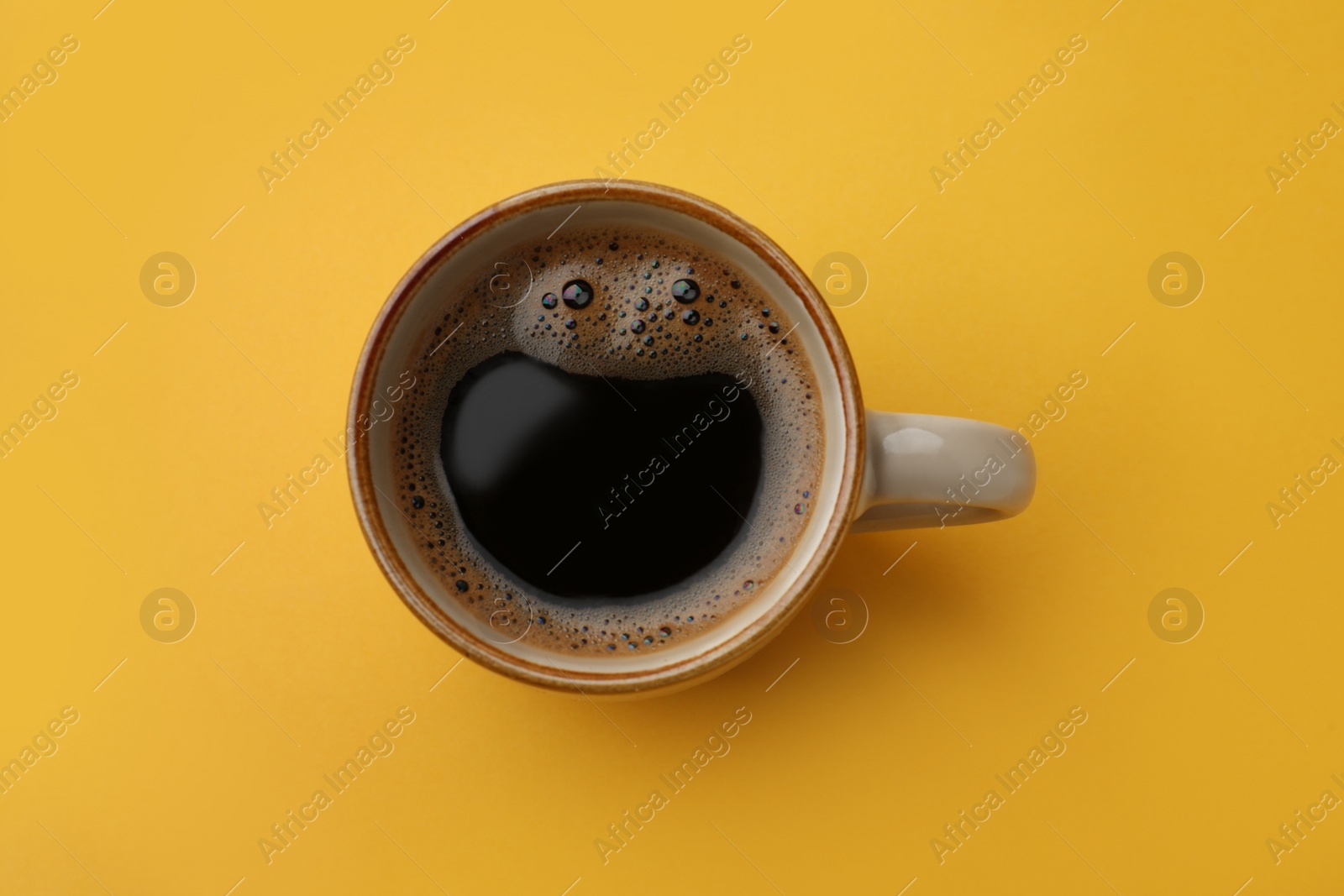 Photo of Cup of delicious black coffee on yellow background, top view