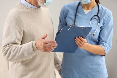 Photo of Nurse with clipboard and elderly patient indoors, closeup