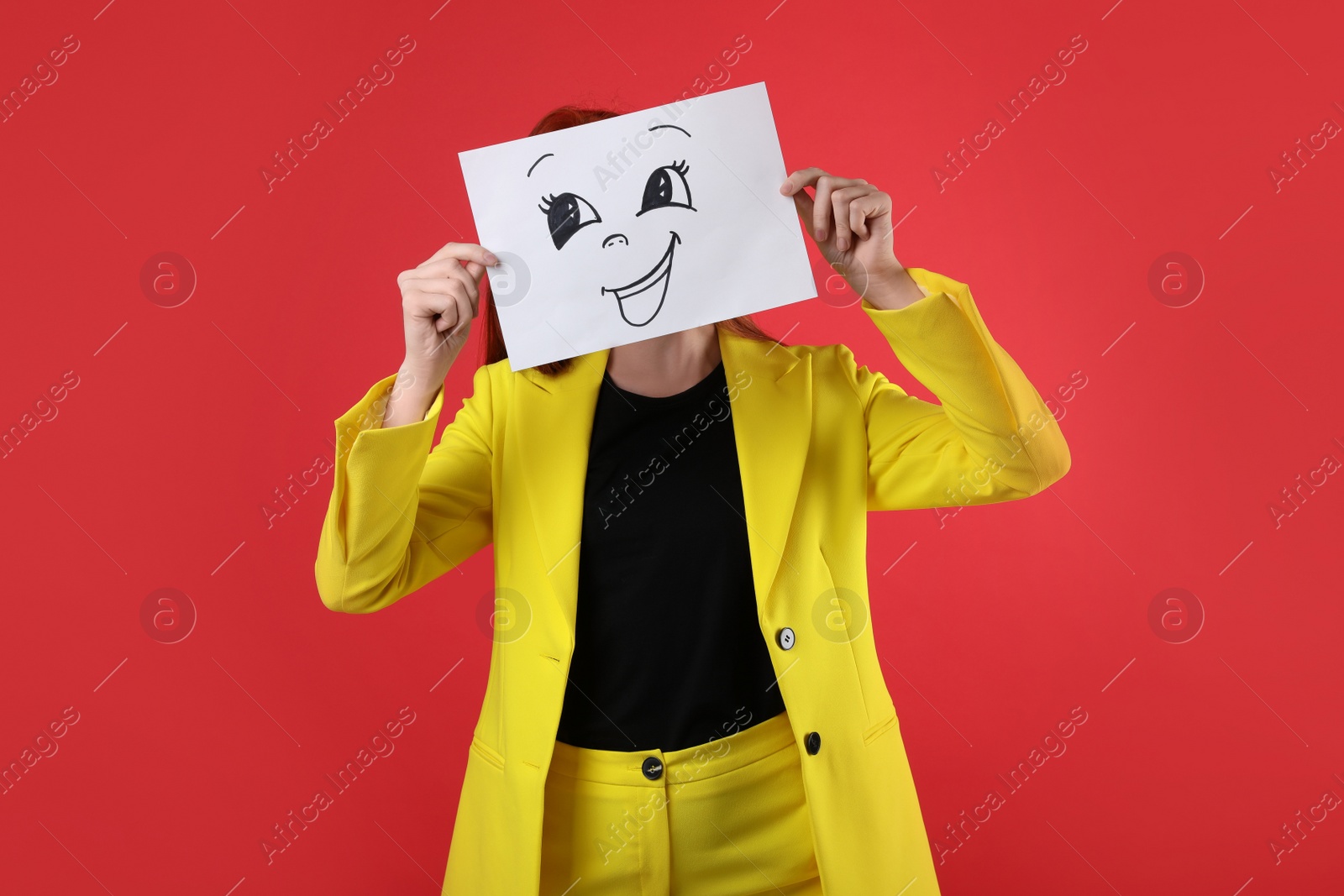 Photo of Woman hiding behind sheet of paper with happy face on red background