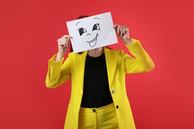 Photo of Woman hiding behind sheet of paper with happy face on red background