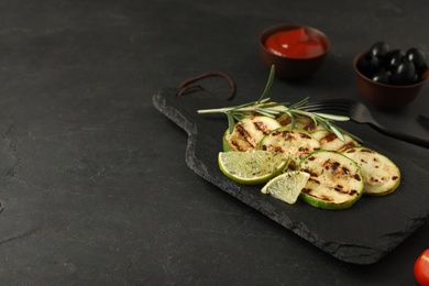 Photo of Delicious grilled zucchini slices served with lime and rosemary on black table. Space for text