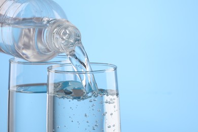 Photo of Pouring water from bottle into glass on light blue background, closeup. Space for text