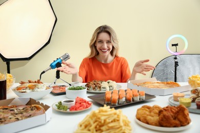 Photo of Food blogger recording eating show near microphone at table against light background. Mukbang vlog
