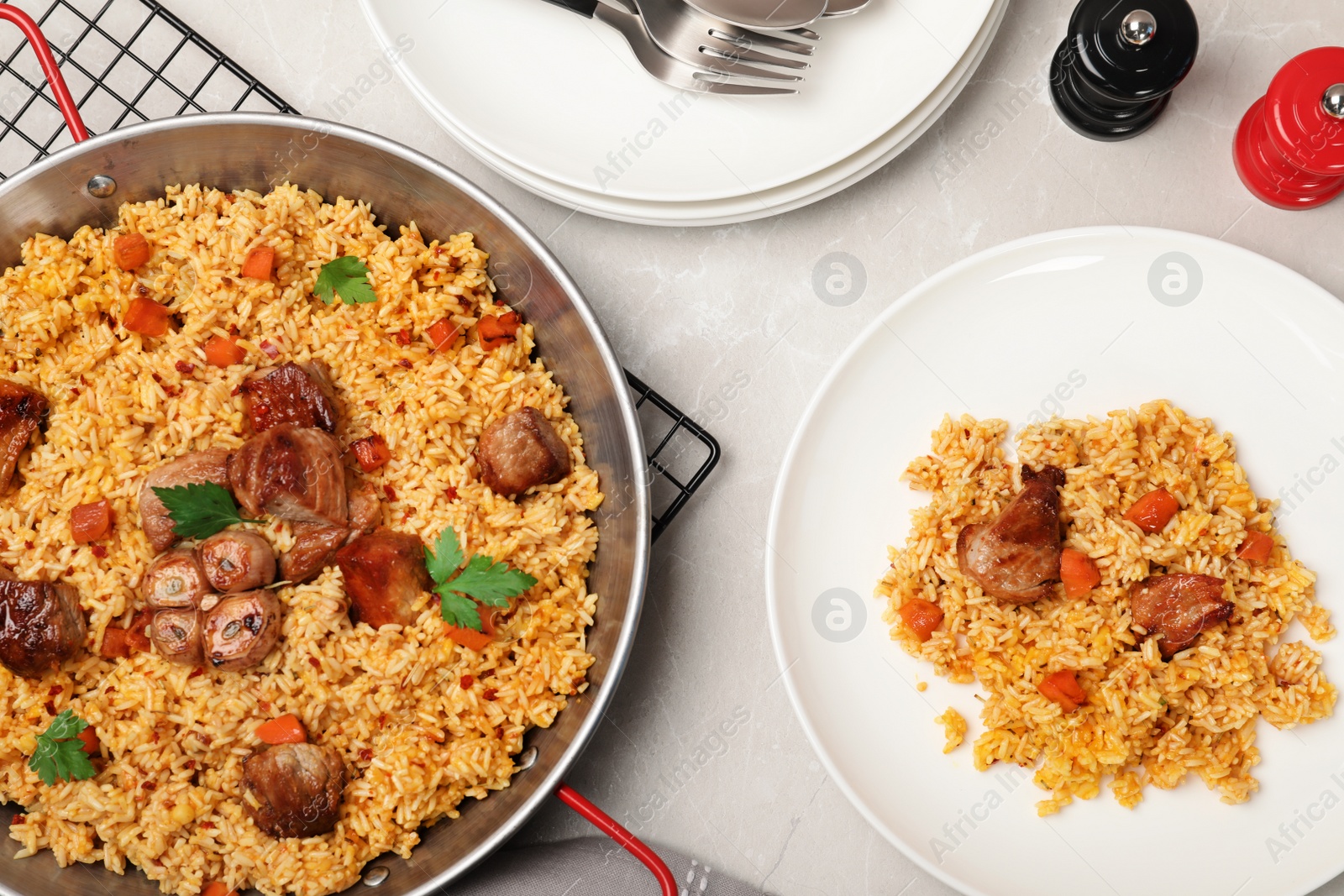 Photo of Frying pan and plate with delicious rice pilaf on light table, flat lay