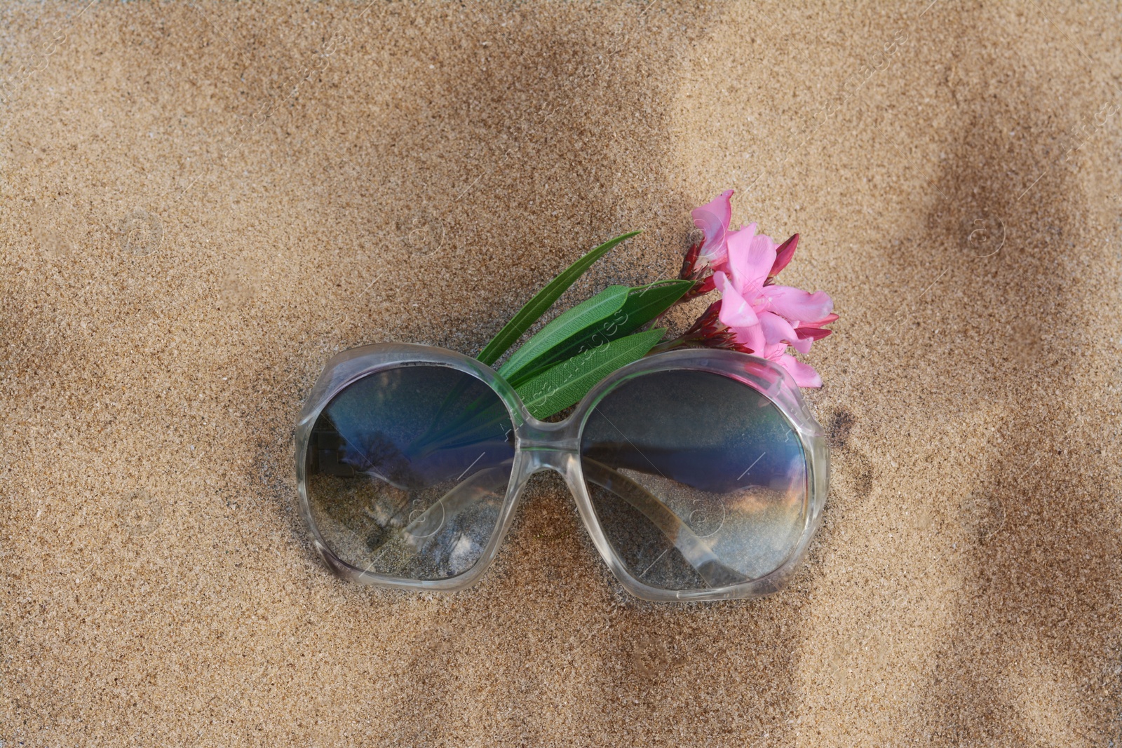 Photo of Beautiful sunglasses with tropical flower on sandy beach, top view
